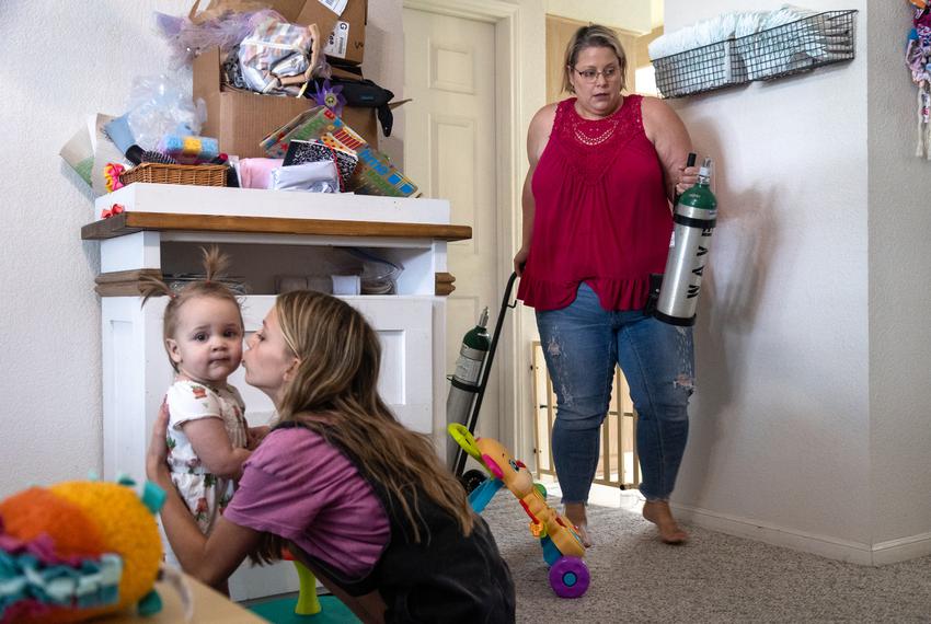 Jodi Whites, 37, grabs oxygen tanks that she used for her daughter Amelia, 3, while her other daughters Avery, 13, and Ali, 14 months, play in their home in New Braunfels, on July 27, 2023. Whites said that the portable oxygen tanks were essential to keeping her Amelia's oxygen levels normal before major surgeries, when her heart issues were at their worst. Without Medicaid coverage, the family had to return the medical equipment to the Pediatric company who owned the gear.