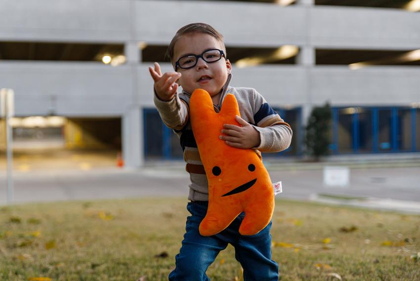 Gabe Nolasco makes a spider web gesture, mimicking his favorite superhero, Spider-Man. In his left hand, he holds onto Thymie, an orange plush thymus, in the yard in front of the Ronald McDonald House at Cook's Children's Medical Center in Fort Worth, Texas on Dec. 2, 2023. Gabe Nolasco, 4, is currently recovering from a thymus transplant as treatment for his congenital athymia.
