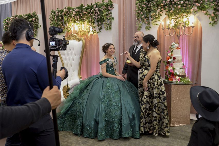 Sienna grins as Troy and Maria Raley give her a bite of cake under the glare of the videographers lights at her Quincenera Saturday, December 16, 2023, in Didoll, Texas.