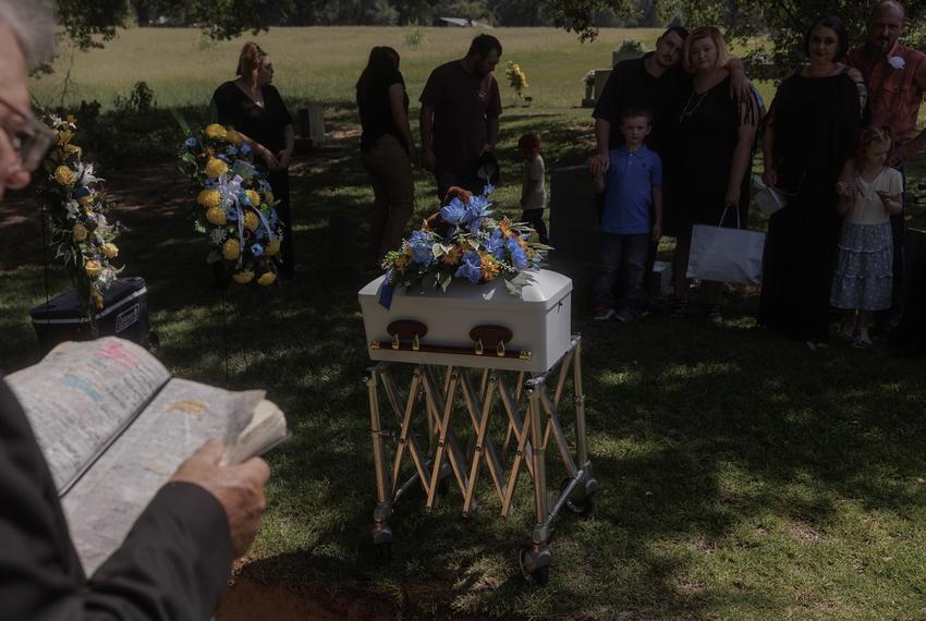 A pastor reads from the bible as family and loved ones gather and embrace each other around the casket carrying Perseus and Helios Langley at a burial in Broken Bow, Oklahoma on August 18, 2023.