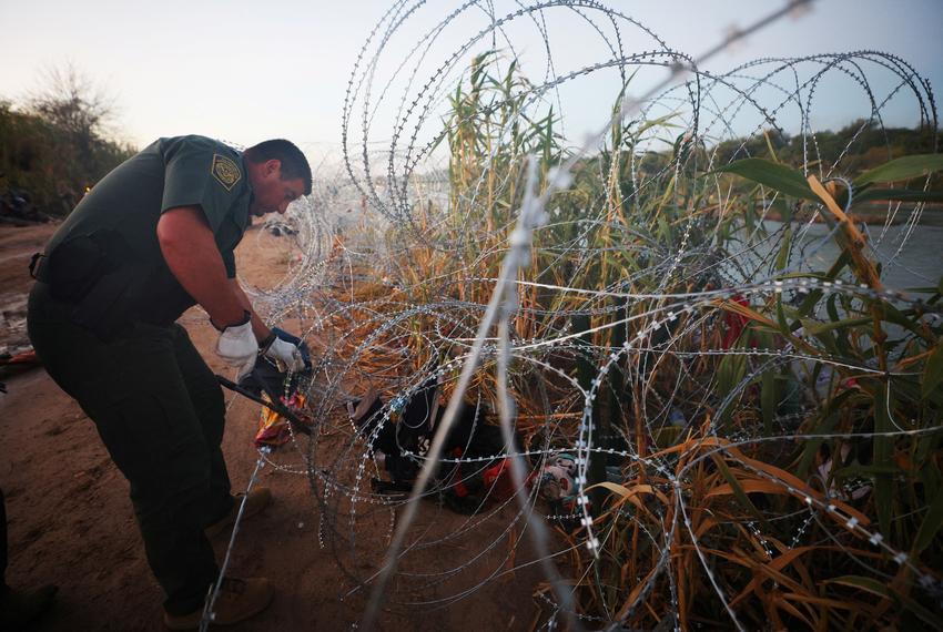 A U.S. Border Patrol agent cuts through razor wire to let in a group of asylum seekers who crossed the Rio Grande in Eagle Pass, Texas, U.S., September 28, 2023.